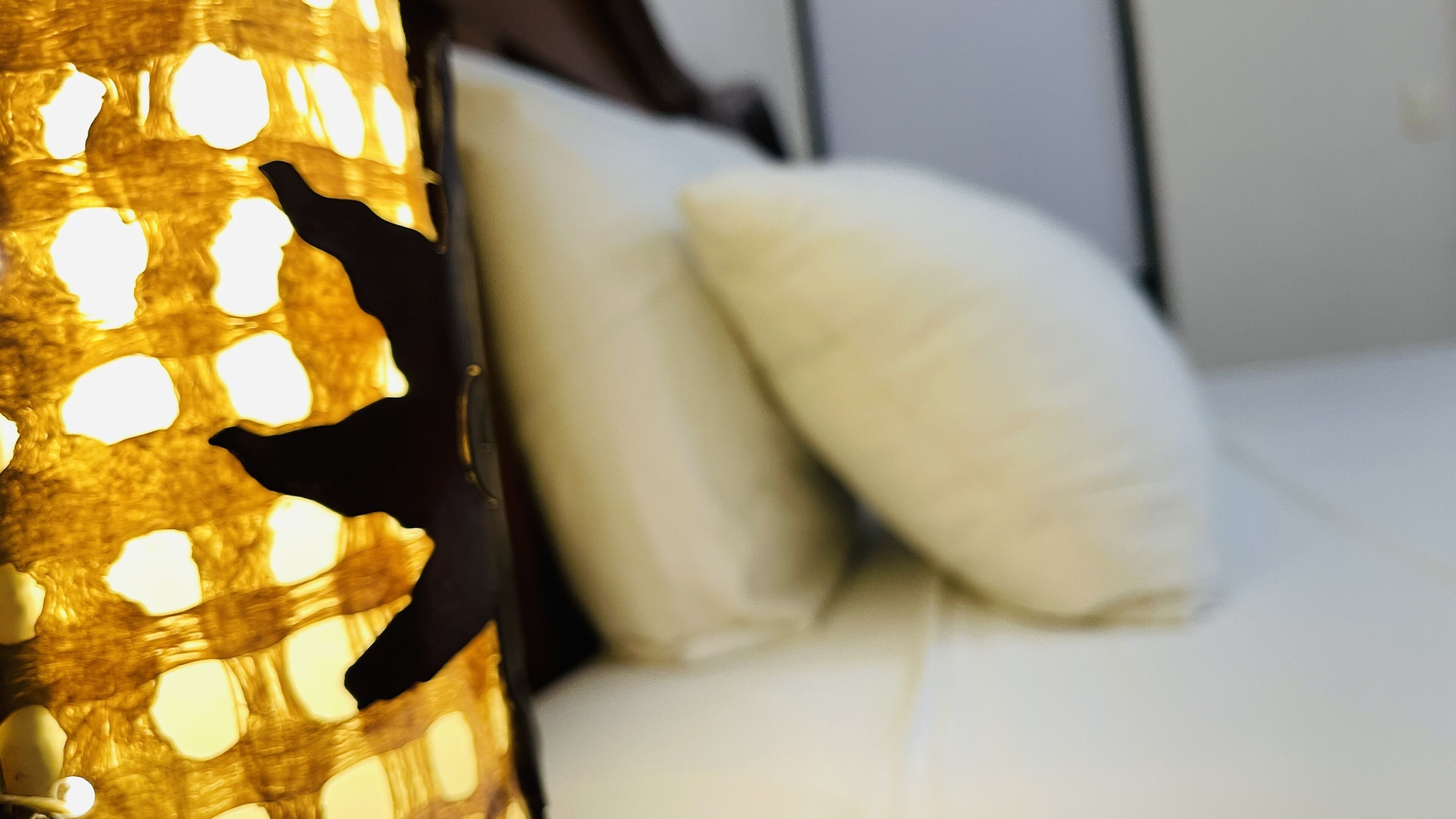 Close-up van een decoratieve lamp met een honingraatpatroon en een wit kussen op de achtergrond.