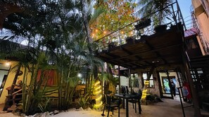 An outdoor seating area with tables and chairs, surrounded by tropical plants and a wooden pergola. - Hotel B&B - 5th Avenue (Playa del Carmen)