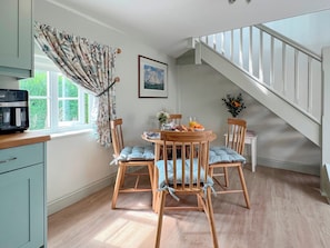 Un coin repas avec une table et des chaises en bois, une fenêtre avec des rideaux, un escalier et un tableau encadré au mur.