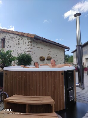 Ein Holzbott mit zwei entspannten Personen, ein Holztisch und eine Terrassenanlage mit einem Metallheizung.
