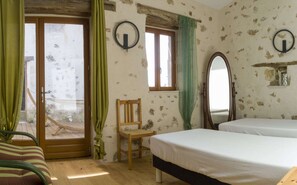 Ein Zimmer mit Holzboden, einem Bett, einem Sessel, einem Fenster mit Vorhängen und einem Spiegel.