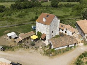 Ein ländliches Steinhaus mit Ziegeldach, umgeben von kleineren Gebäuden und einer Feldweg.