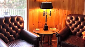 A room with wooden walls, two leather armchairs, a small round table with a lamp, and a view through a glass door. - Mount Snow Vermont - Ski - Snowboard - 6 miles (Wilmington)