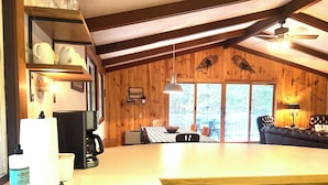 A kitchen with wooden cabinets, a sink, and a dining area with a table and chairs. - Mount Snow Vermont - Ski - Snowboard - 6 miles (Wilmington)
