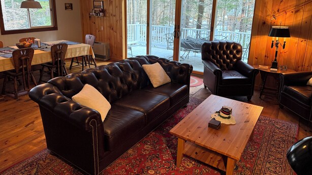 A cozy living room with a leather sofa, a wooden coffee table, and a dining area with a table and chairs. - Mount Snow Vermont - Ski - Snowboard - 6 miles (Wilmington)
