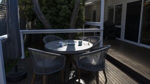 A covered outdoor patio with a round table and four wicker chairs, surrounded by a wooden deck and a white railing. - Relax in this boho coastal home walking distance to beautiful beach (Blairgowrie)
