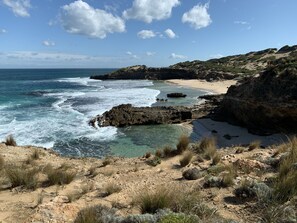 Eine Küstenlandschaft mit felsigem Gelände, klarem blauen Wasser und einem Sandstrand.