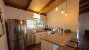 A modern kitchen with a stainless steel refrigerator, a dishwasher, a stove, and a large island with bar stools. - Relax in this boho coastal home walking distance to beautiful beach (Blairgowrie)
