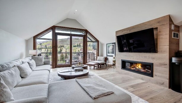 Un salón amplio con un sofá grande, una chimenea y un televisor montado en la pared.