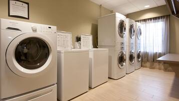A laundry facility with multiple washing machines and dryers, a 'Free Guest Laundry' sign, and a tiled floor.