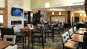 Eine Hotelhalle mit mehreren Sitzbereichen, einem Kamin, einem Fernsehbildschirm und einer Rezeption.