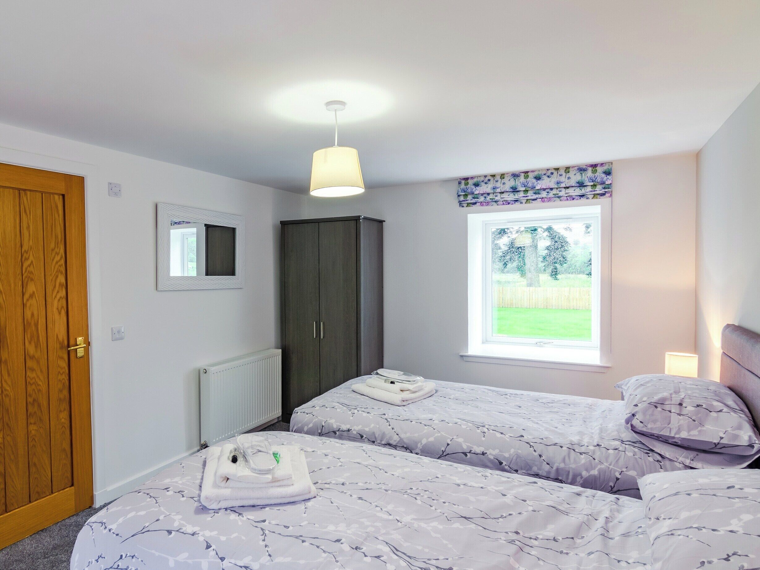 A bedroom with two beds, a wardrobe, a radiator, a window with a view of the outdoors, and a hanging light fixture.