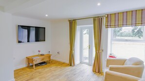 Ein modernes Wohnzimmer mit Holzboden, einer Couch, einem Couchtisch und einem an der Wand montierten Fernseher.