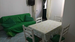 A room with a green sofa, a white table with a floral tablecloth, and white chairs. - Sandra's House in Meta di Sorrento (Meta)