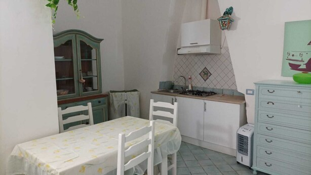 A small kitchen with a table and chairs, a cabinet, a stove, and a radiator. - Sandra's House in Meta di Sorrento (Meta)