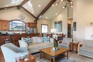 A spacious living area with a high ceiling, wooden beams, and a large window offering a view of the outdoors. There are multiple seating options including a sofa, chairs, and a coffee table. - Fairway Ski and Golf Retreat by Avantstay Blocks From the Ski Lift! Beautiful Views w/ Hot Tub (Park City)