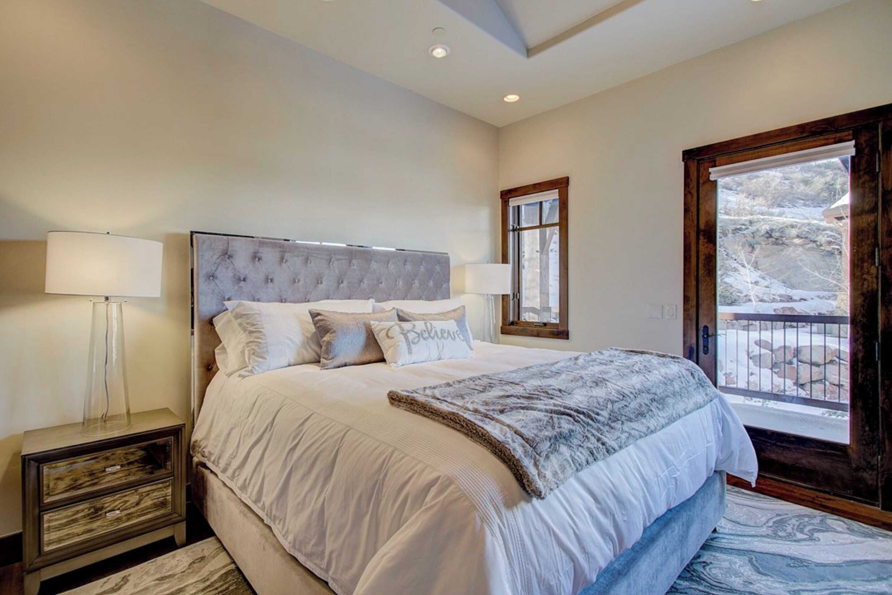 A bedroom with a large bed, two bedside tables, a window with a view, and a balcony.