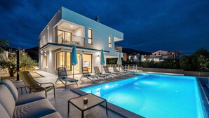 En moderne bygning med to etager, en swimmingpool, udendørs siddepladser og en balkon.