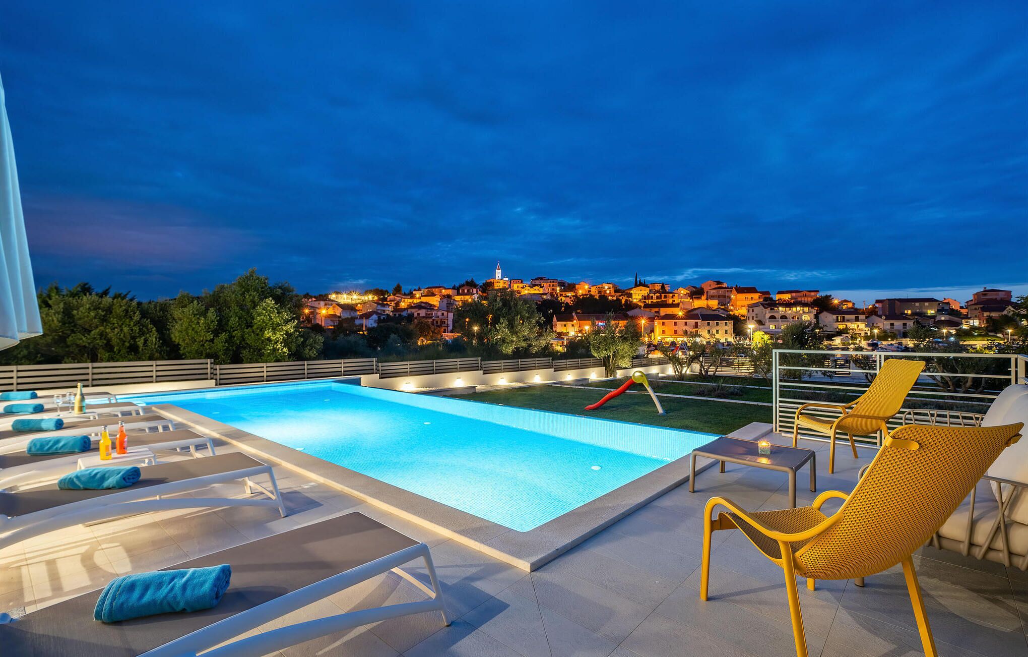 Una piscina en la azotea con sillones de descanso y vistas a un pueblo al atardecer.