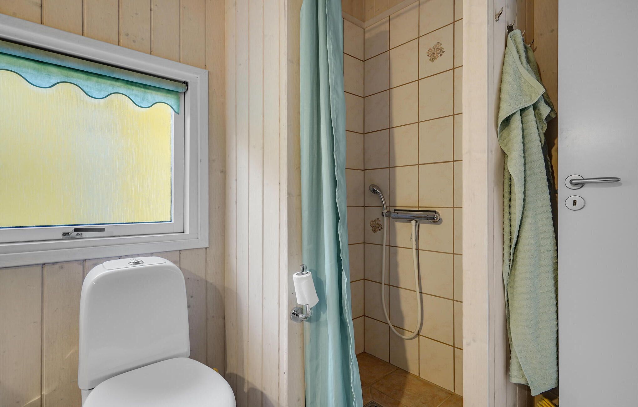 A bathroom with a toilet, a shower with a curtain, and a towel hanging on the door.