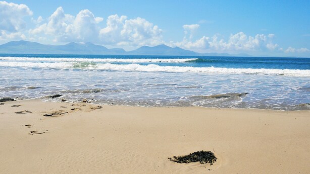 Una spiaggia con le onde, un cielo sereno e montagne sullo sfondo.