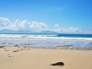 A beach with waves, a clear sky, and mountains in the distance.