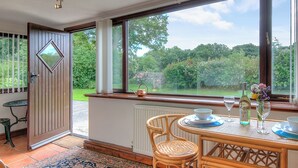 Zona pranzo con tavolo apparecchiato per due, vista sul giardino attraverso ampie finestre e porta che dà all'esterno.