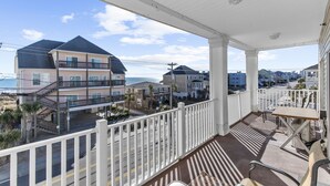 Ein Balkon mit Blick auf Strand und Meer, ein weißes Geländer und ein Tisch mit Stühlen.