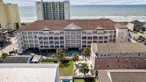 Ein mehrstöckiges Hotel mit Pool und Blick auf Strand, umgeben von anderen Gebäuden und dem Meer.
