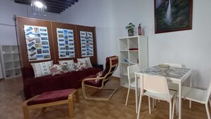 A living room with a red sofa, a wooden chair, a white table, and a bookshelf. - Study Cádiz center, meters with air conditioning. Up to 5 people (Cádiz)