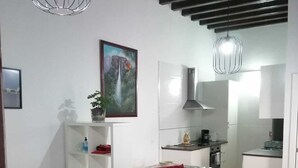 A living room with a red sofa, a white coffee table, and a wooden chair with a cushion. There is a painting on the wall and a kitchen in the background. - Study Cádiz center, meters with air conditioning. Up to 5 people (Cádiz)