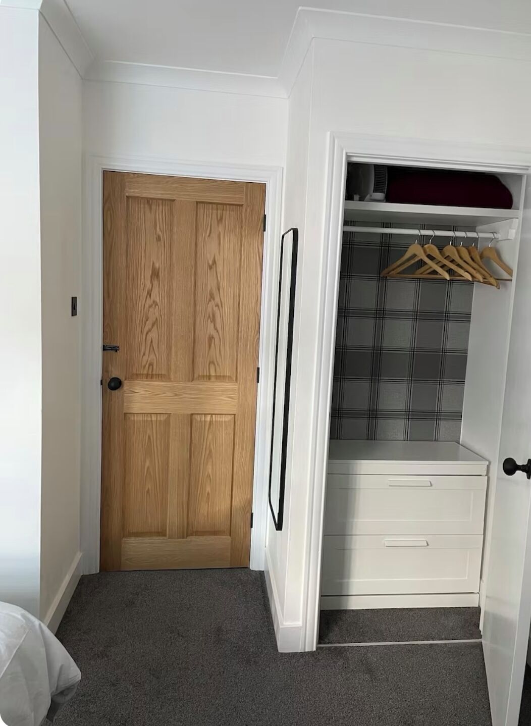 A walk-in closet with a wooden door, a hanging rod, and a plaid-patterned wall.