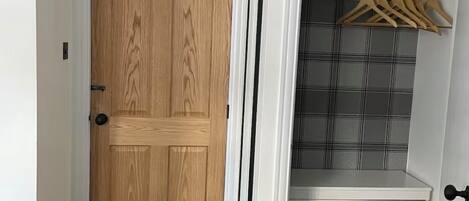 A walk-in closet with a wooden door, a hanging rod, and a plaid-patterned wall.