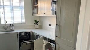 A compact kitchen with a built-in washer and dryer, a window with blinds, and a small potted plant. - Freshly updated town house Carlisle City Centre (Carlisle)