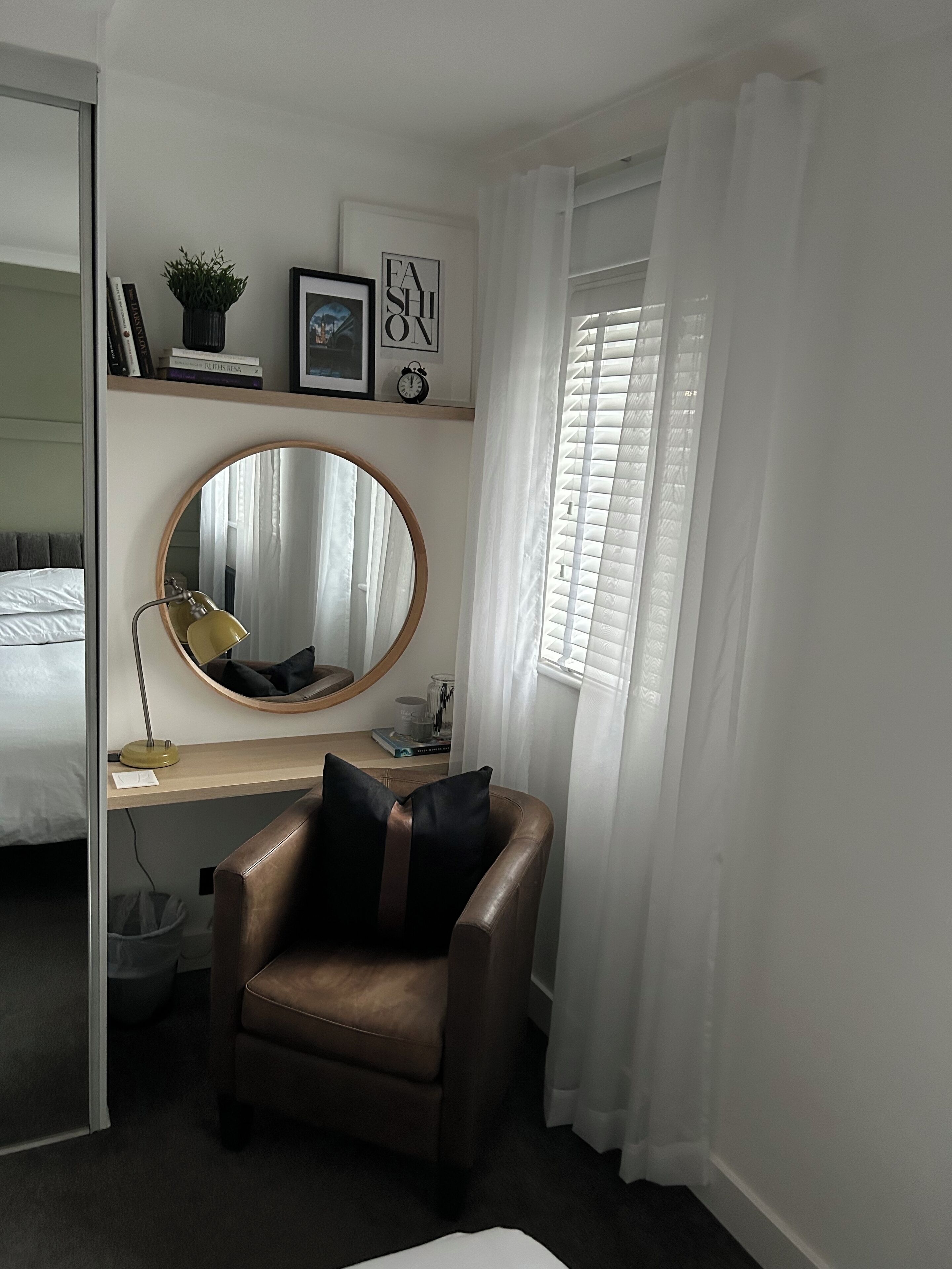 Een slaapkamer met een bed, een bureau met een spiegel, een stoel en een raam met gordijnen.