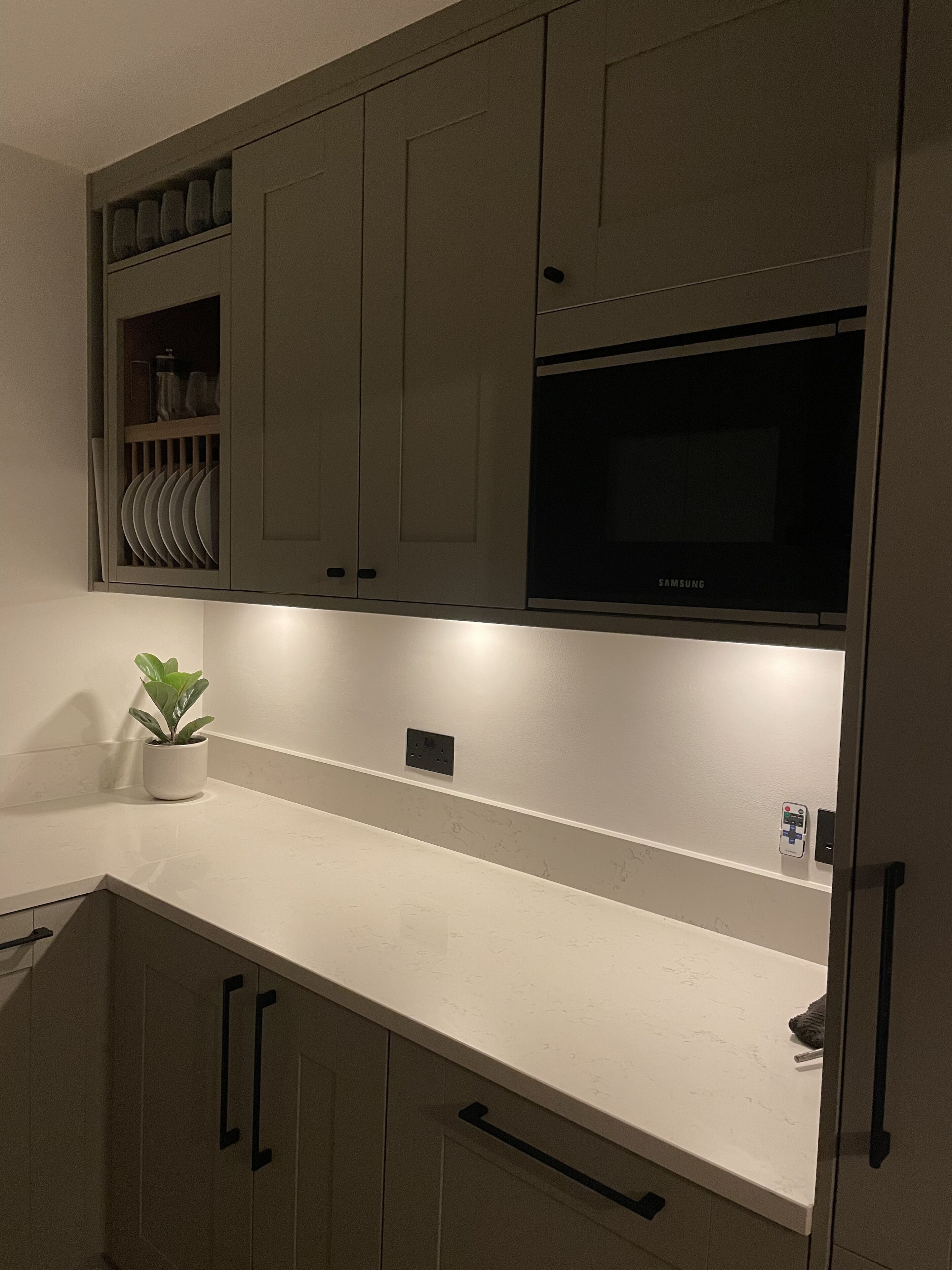 Une cuisine moderne avec des meubles gris, un plan de travail blanc et un four à micro-ondes encastré.