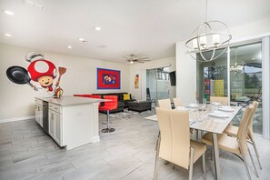 A modern kitchen with a central island, a dining area with a glass table, and a living space with a sofa and a red accent wall.
