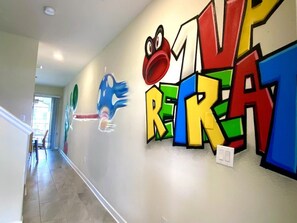A hallway with colorful graffiti art on the wall, including a large number '1' and a cartoon frog. - 1upRetreat - Mario Private Pool Lazy River Disney (Davenport)