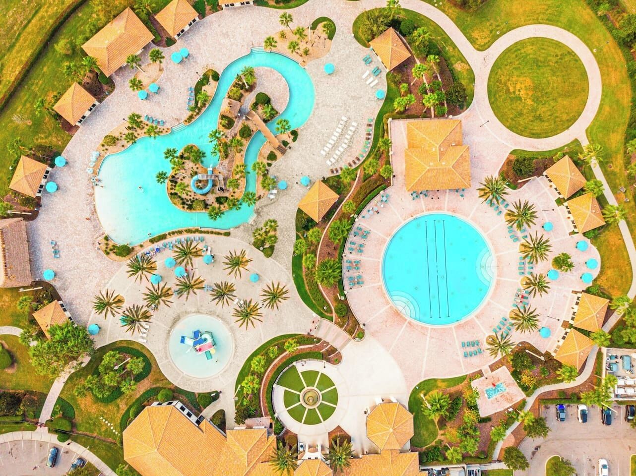 Vista aérea de un resort con varias piscinas, tumbonas y palmeras.