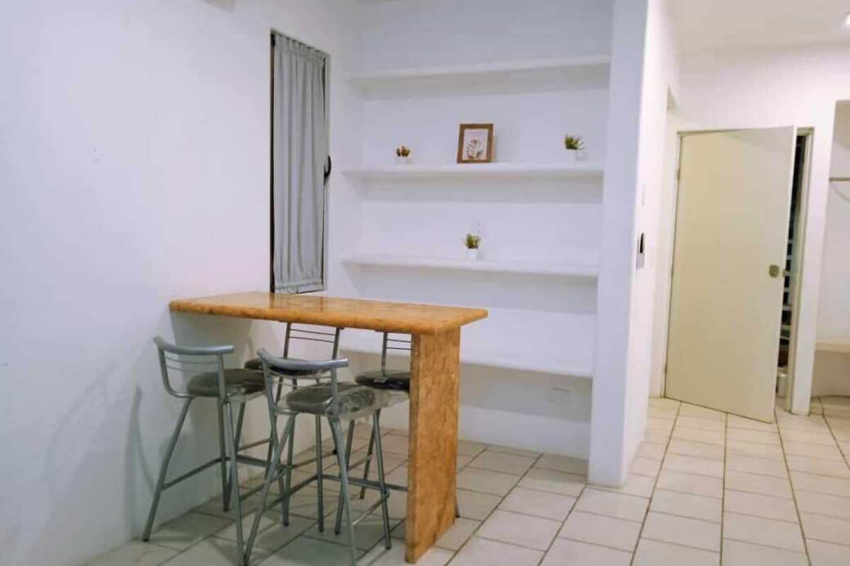 Une petite cuisine avec une table en bois et deux tabourets en métal. Au-dessus du comptoir, on trouve des étagères blanches ornées de petits objets décoratifs.