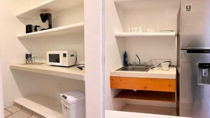 A compact kitchen with white cabinets, a microwave, a sink, and a stainless steel refrigerator.