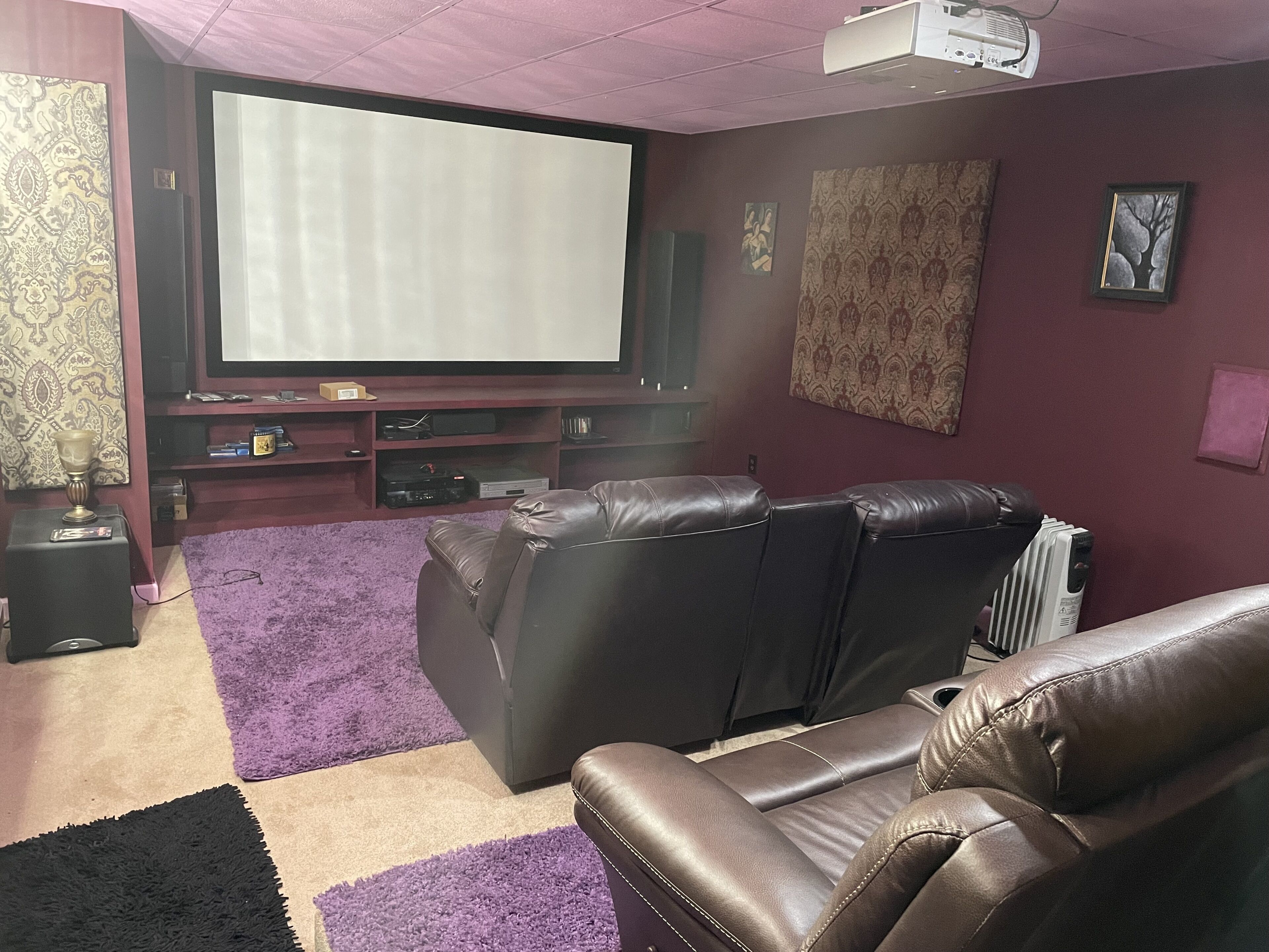 A living room with a large flat-screen TV, leather sofas, a purple rug, and a projector.