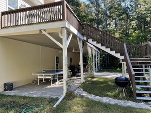 A covered outdoor area with a wooden deck, a barbecue grill, and a ping pong table.