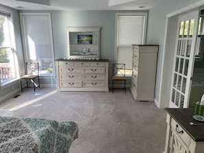A bedroom with a large window, a dresser, a chair, and a bed.