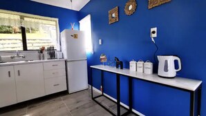 Una cocina con armarios blancos, una pared azul y un ventanal con vistas a zonas verdes.
