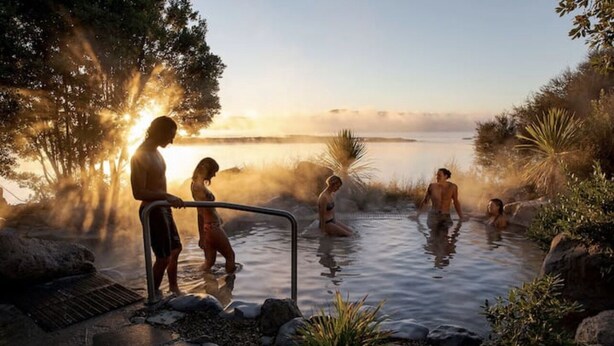 Una fuente termal natural con gente relajándose en el agua, rodeada de rocas y vegetación.