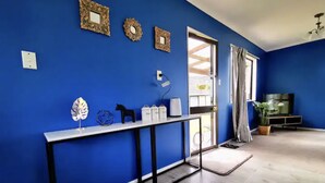 Una habitación con paredes azules, suelo de madera, una mesa consola con adornos, un televisor y una ventana con cortinas.