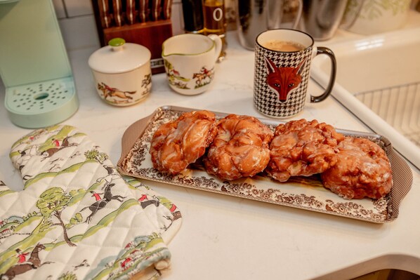 A tray of pastries on a table with a floral-patterned cloth, a patterned napkin, and a mug with a fox design.