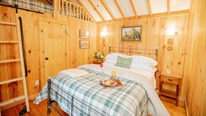 A wooden-paneled bedroom with a bed, a nightstand, a ladder, and a painting on the wall.
