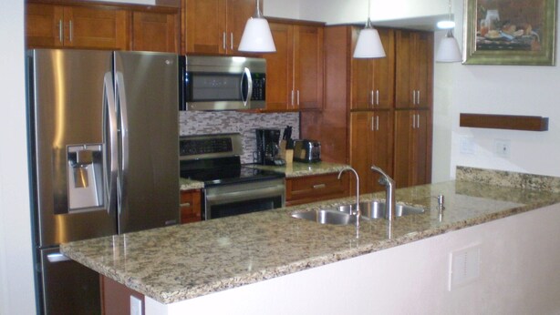 A kitchen with stainless steel appliances, granite countertops, wooden cabinets, and pendant lighting. - Peaceful and tranquil townhouse for seniors  Heated pool/Spa gym. covered patio (Mesa)